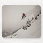 A snowboarder jumps off a cliff into powder in mousepad