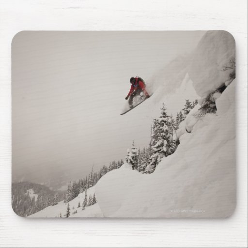 A snowboarder jumps off a cliff into powder in mousepad