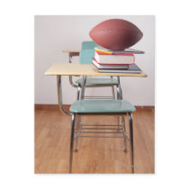 A student desk with a football sitting on a pile post cards