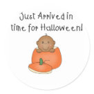 round_sticker - An adorable African American baby sits inside an orange pumpkin and kid style text reads "Just arrived in time for Halloween!" on babys 1st Halloween T-shirts, tote bags, magnets, and more.: Sizes 