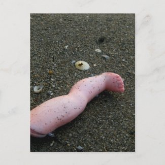 Beach pollution broken doll leg on sand postcard