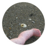 Beach pollution broken doll leg on sand round sticker