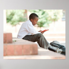 Boy reading on steps outside school, posters