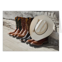 Cowboy hat on row of cowboy boots outside a log greeting card