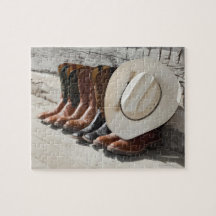 Cowboy hat on row of cowboy boots outside a log puzzle