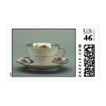 Cup and saucer with colorful flower designs on it. postage