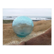 Glass float on sand at beach postcard