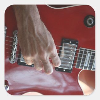 Hand playing red electric guitar near pickup sticker