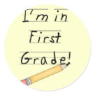 round_sticker - Cute 1st grade design for kids in first grade appears to be lined paper and printing with a big yellow pencil. Text reads "I'm in First Grade!".