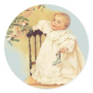 round_sticker - An infant gazes in wonder at decorations hanging from the Christmas tree. A stocking is clutched in babys hand while holding tightly to a chair with the other. First Christmas 2007 text on baby clothing.: Sizes 