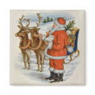 square_magnet - Santa is standing beside his Reindeer offering a cube of sugar to the closer one. His sleigh is full of gifts and toys. Snow covered hill are the background.: Sizes 