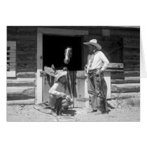 Two cowboys standing next to a barn with a horse cards