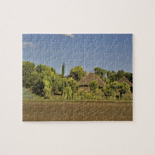 A farmed field in front of thatched roof houses jigsaw puzzle