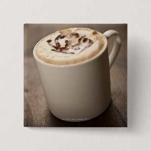 A mug of Cappuccino coffee topped with melted Pinback Button