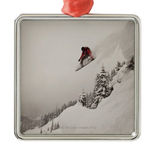 A snowboarder jumps off a cliff into powder in metal ornament