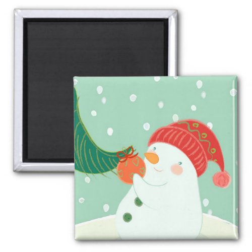 A snowman hanging an ornament on a tree magnet