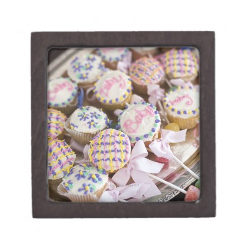 A tray of baby rattle cupcakes at a baby shower gift box