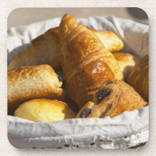 A wicker breakfast basket with croissants, and drink coaster