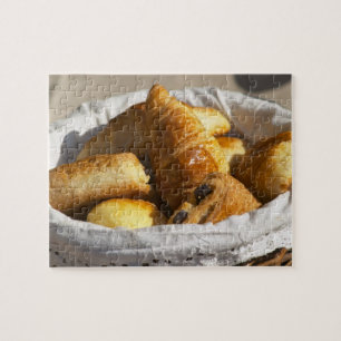 A wicker breakfast basket with croissants, and jigsaw puzzle