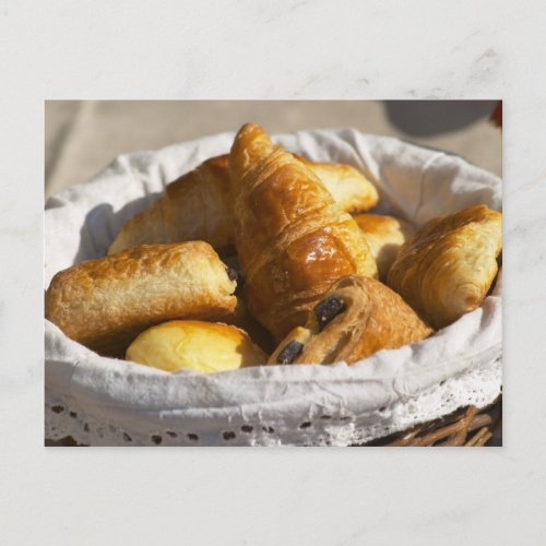 A wicker breakfast basket with croissants and postcard