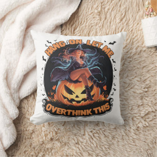A witch playfully pondering atop a pumpkin throw pillow