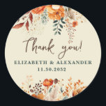 Autumnal names and wedding date floral thank you classic round sticker<br><div class="desc">These romantic and elegant autumnal floral Thank-you stickers make the perfect seal for your wedding favor, presenting a chic botanical design that features a classy watercolor illustration of flowers and greenery in warm fall tones and is easily customizable with your names and wedding date. These stickers are part of the...</div>