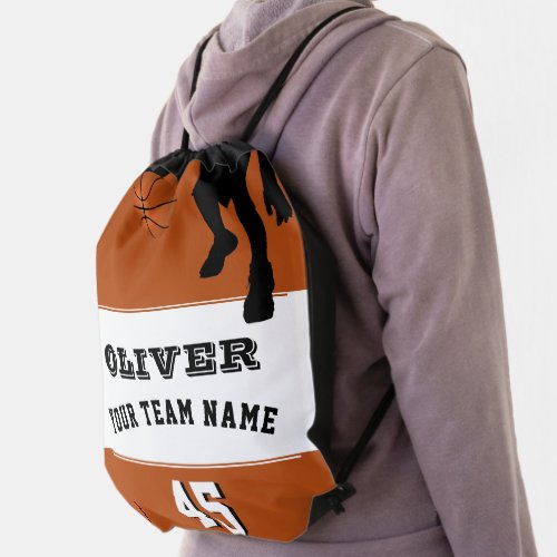 Basketball Player Team Name Number Drawstring Bag - Basketball Player Team Name Number Drawstring bag. The design has a black silhouette of a basketball player with a basketball on orange background. The text is in modern fonts - personalize it with your team name, number and your name. Perfect for basketball players or a keepsake to remember your favorite sport.