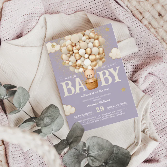 A classic baby shower invitation is resting on top of a baby onesie with a light pink baby blanket underneath. A single piece of eucalyptus is placed on top of the display!
