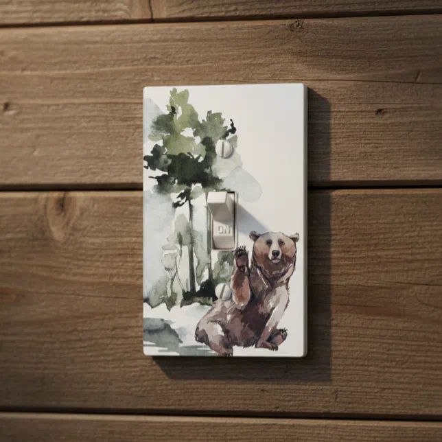 A light switch cover with some abstract art of a bear and trees. It is placed on a dark wooden wall.