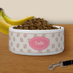 Beige And Pink Dog Paws Pattern With Custom Name Bowl<br><div class="desc">Beige dog paw print pattern background with a pink badge that has a personalizable text area for the name of the pet. The font is a lovely script font in white color.</div>
