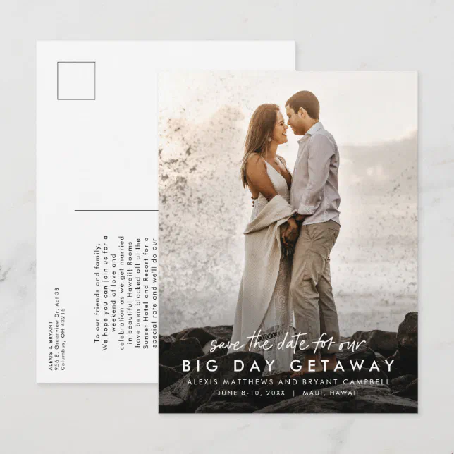 A destination wedding invitation postcard showing a picture of the engaged couple standing by the shoreline as a large wave splashes in the background.