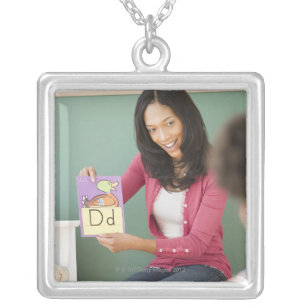 Black teacher showing letter d flash card to silver plated necklace