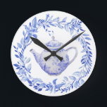 Blue and White Tea Pot with Wreath  Round Clock<br><div class="desc">This tea pot clock has a monochromatic design featuring a blue and white tea pot surrounded by a wreath of blue leaves. This clock would be a perfect gift for any tea lover.</div>