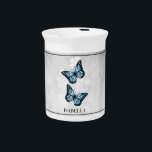 Blue Butterfly Floral Beverage Pitcher<br><div class="desc">Serve your hot or cold beverages with this unique Blue Butterfly Floral Personalized Porcelain Pitcher. Pitcher design features a pair of vibrant butterflies resting on a white floral vine against a light gray grunge background. Additional gift items available with this design as well as a variety of colors.</div>