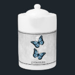 Blue Butterfly Floral Teapot<br><div class="desc">Enjoy your tea with a Blue Butterfly Floral Personalized Teapot.  Teapot design features a pair of vibrant butterflies resting on a white floral vine against a light gray grunge background. Additional gift items available with this design as well as a variety of colors.</div>