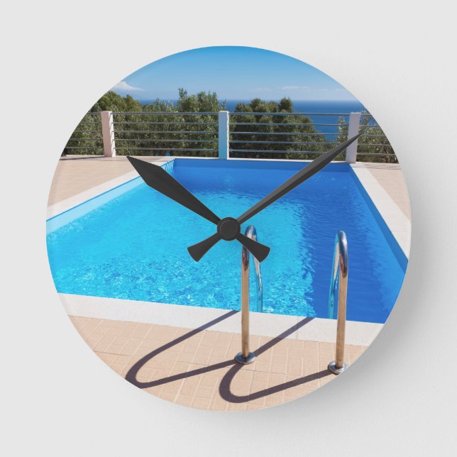 Blue swimming pool with steps at sea round clock (Front)