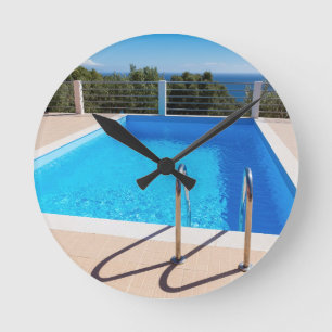 Blue swimming pool with steps at sea round clock