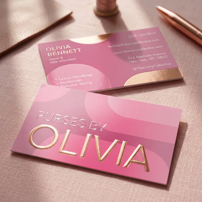 A pink and gold spot UV business card is lying next to a pen and pencil, with the light reflecting on the gloss.