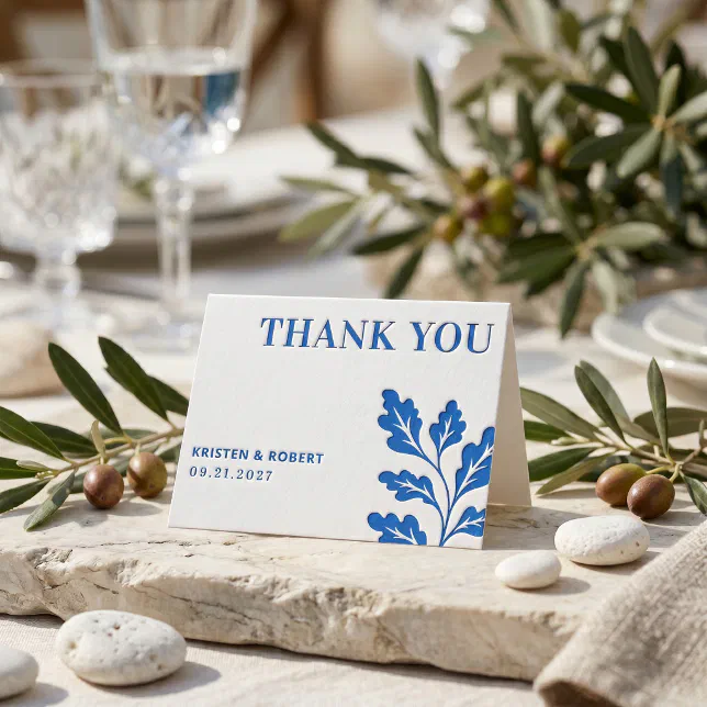 A folded thank you card is seen surrounded by rocks and greenery, with two wine glasses in the background.