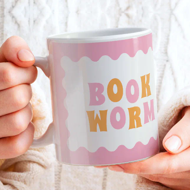 A person in an Aran jumper is holding a pink and orange mug with a book-themed design.