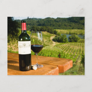 Bottle of red wine and glass on table postcard