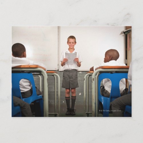 Boy standing in front of class reading in postcard