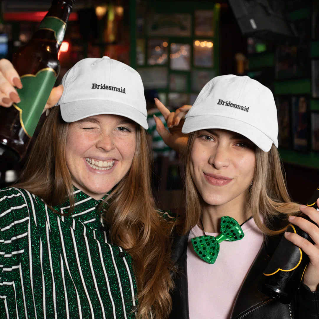 Two girls partying and wearing bridesmaid embroidered baseball hats.