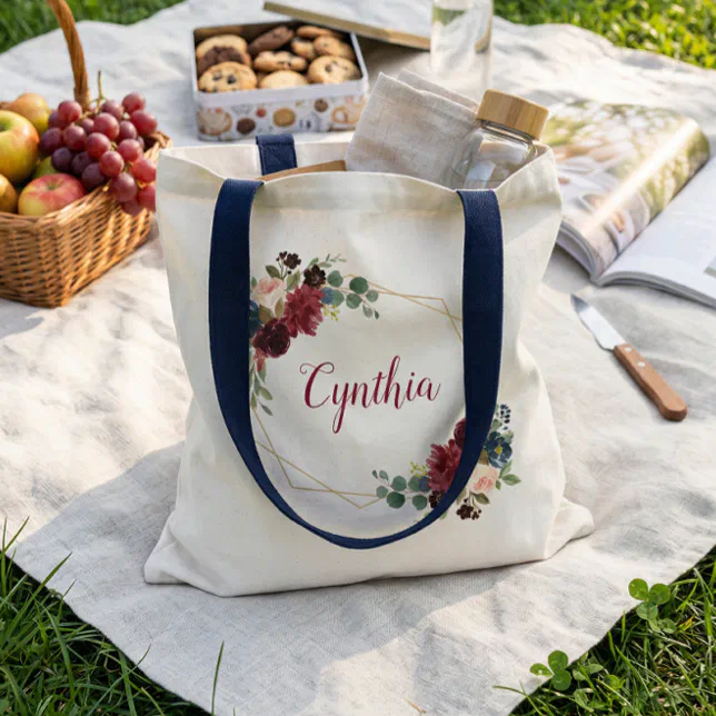 A monogrammed tote bag with a floral motif. Food items are scattered around the bag.