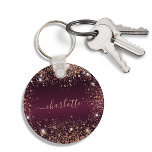 Burgundy rose gold glitter name script keychain<br><div class="desc">A burgundy faux metallic looking background color. Decorated with rose gold faux glitter dust. Personalize and add a name. The name is written with a modern hand lettered style script with swashes. To keep the swashes only delete the sample name, leave the spaces or emoji's in front and after the...</div>