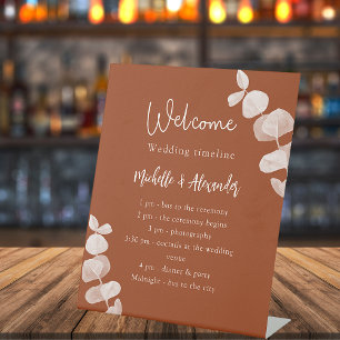 Burnt orange eucalyptus wedding program timeline pedestal sign