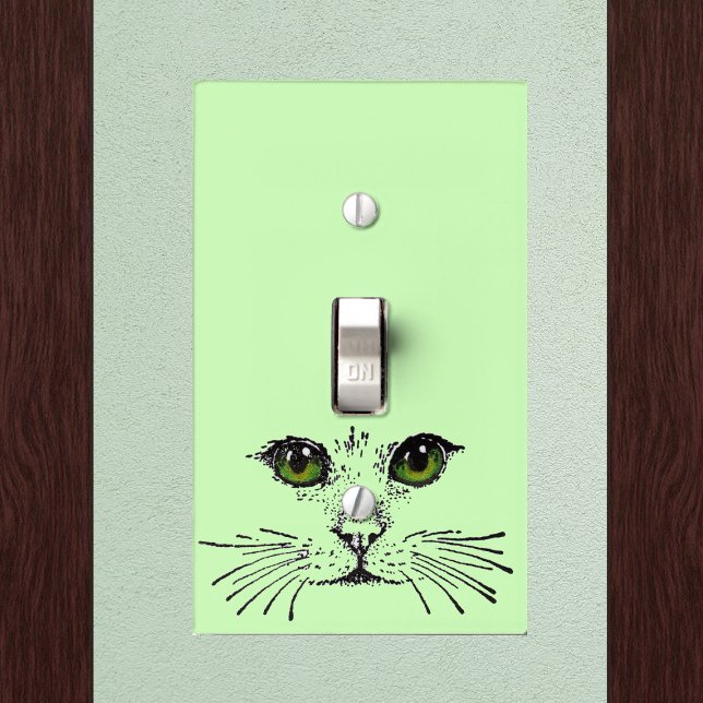 Cat Face Green Eyes Whiskers Light Switch Cover (Black drawing of cat face with whiskers green eyes on light green electrical wall plate.)