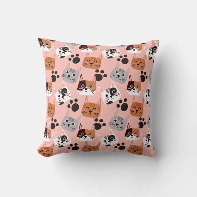 Cat Faces Throw Pillow (A flat lay shot shows a square pillow with a pink background and a repeating pattern of cartoon cat.)