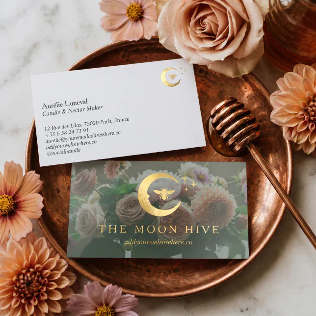 A set of elegant, vintage floral business cards featuring a gold foil crescent moon and bee logo resting on a copper tray surrounded by peach and pink dahlia and cosmos flowers.