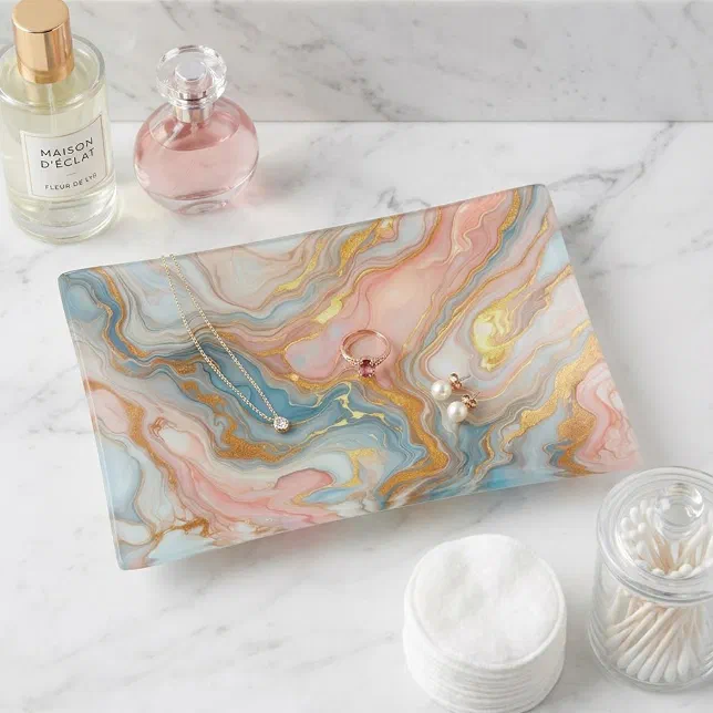 A pink, gold and blue marble-style trinket tray holds some earrings, a necklace and a ring. In the background there is two perfume bottles.
